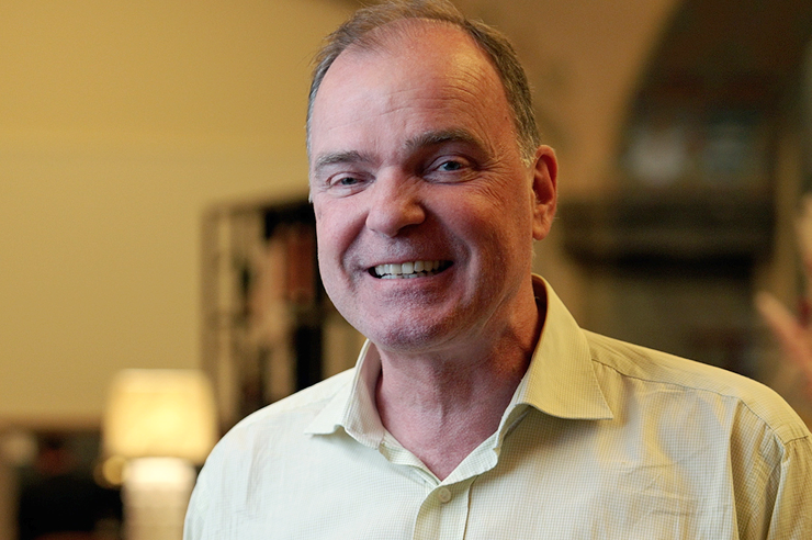 En leende man med kort brunt hår klädd i en ljus skjorta med knappar.