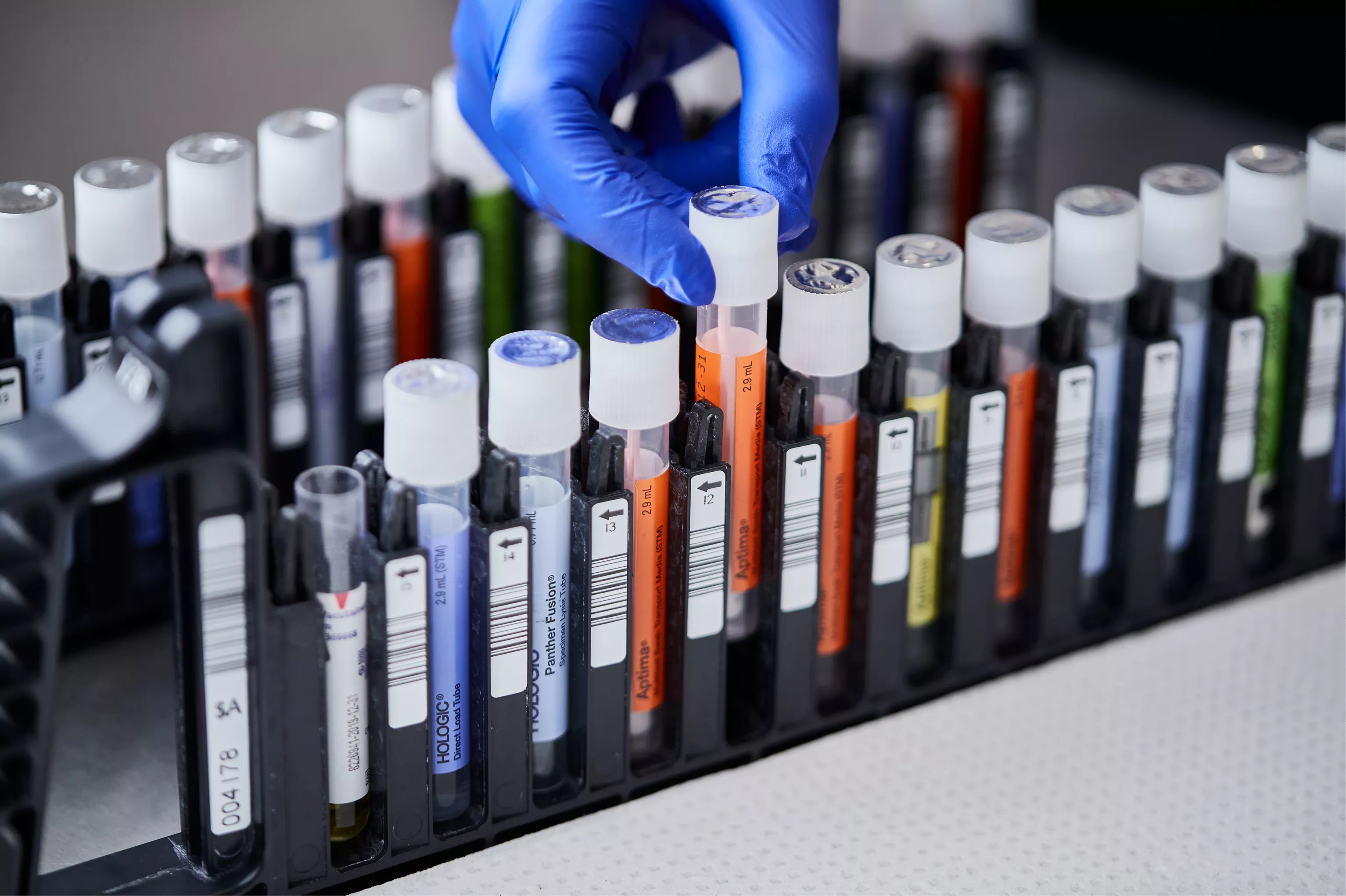 Behandskad hand tar ut provburk från bricka